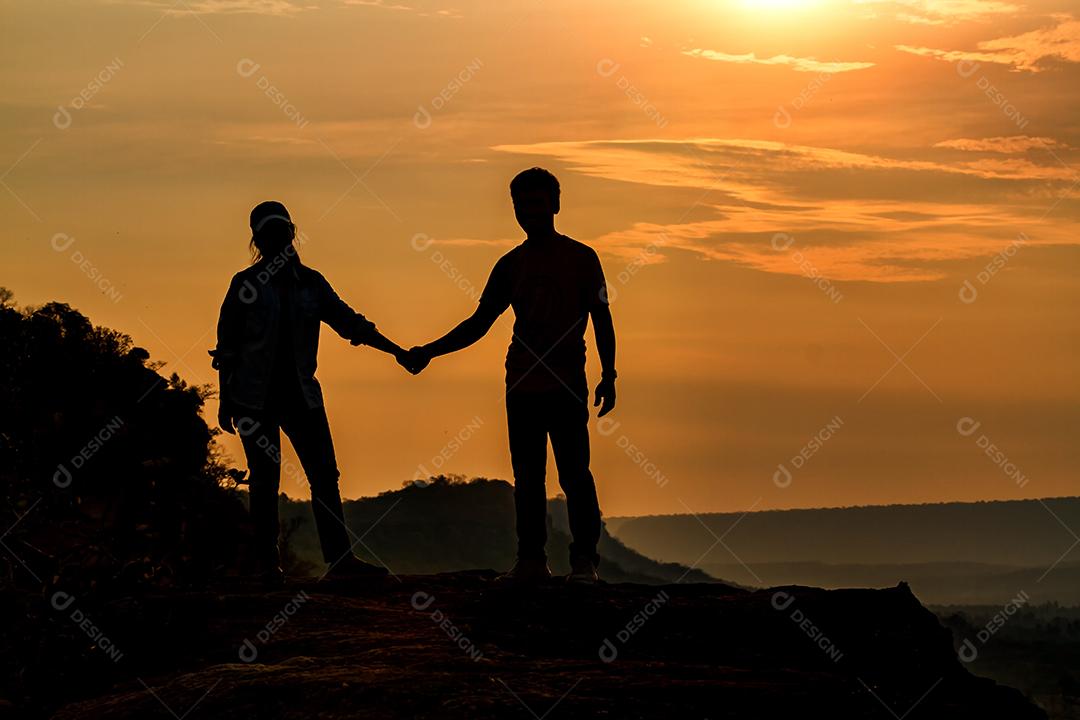 Casal de silhueta segurando a mão para viajantes no nascer do sol