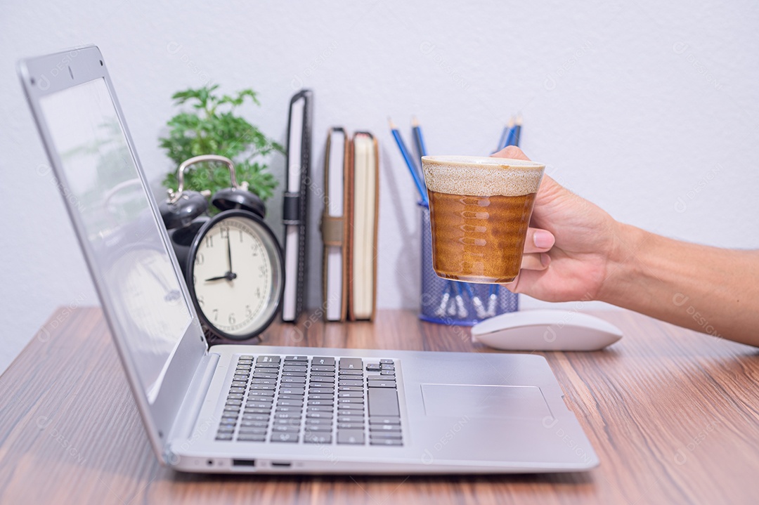 Mão segurando a xícara de café na frente do notebook