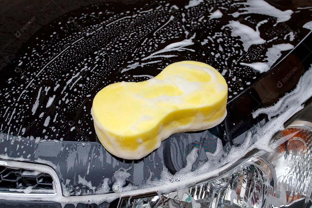 mão do homem lavando o carro usando a esponja amarela com espuma