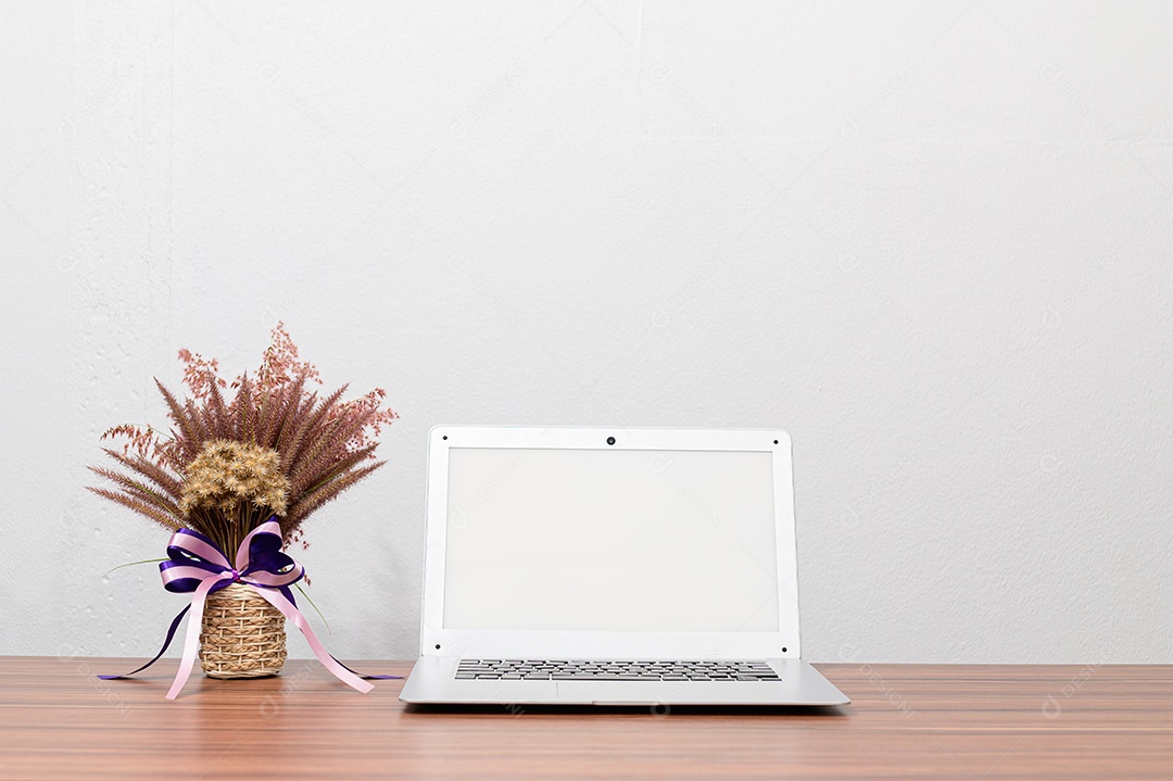 Computador, notebooks e vasos de flores estão em sua mesa.