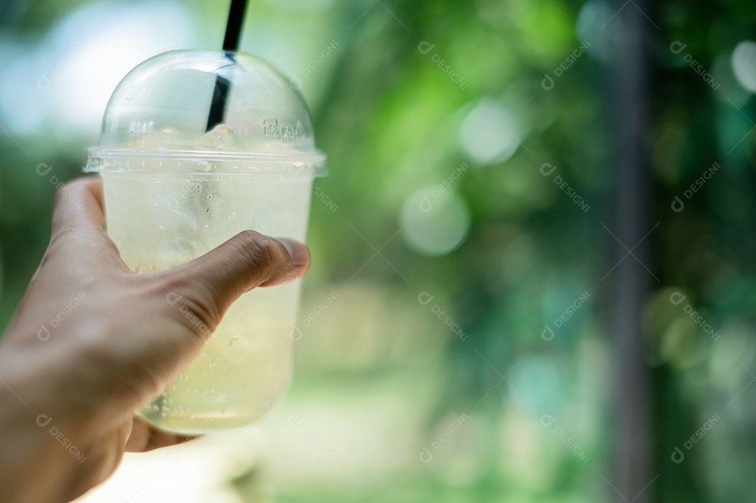Mão segurando um copo de água, o sabor do suco de limão misturado com mel.