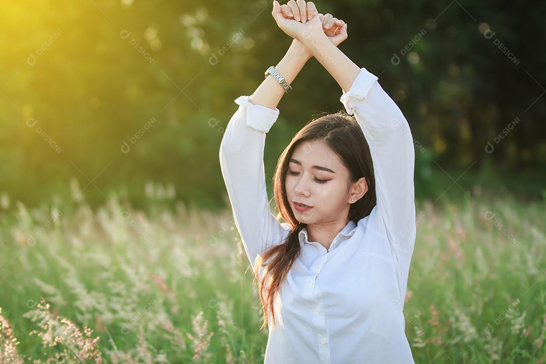 Mulher relaxante no prado de grama verde no pôr do sol de verão e descansando linda jovem caucasiana asiática multicultural