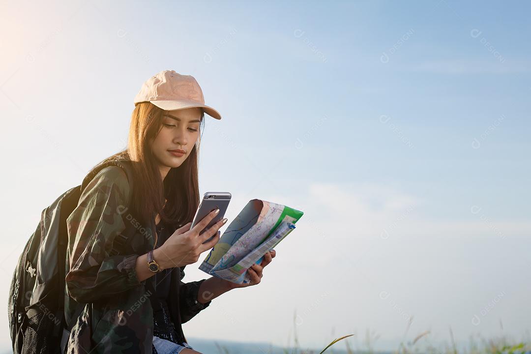 mulheres asiáticas com mochila brilhante olhando para um mapa. Vista de trás do viajante turístico na montanha de fundo, mãos femininas usando smartphone, segurando gadget