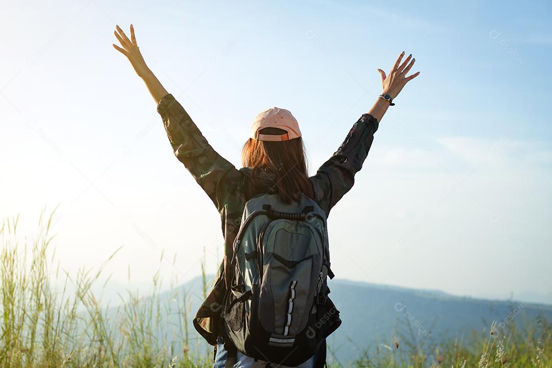 Mulher viajante da liberdade de pé com os braços levantados e desfrutando de uma bela natureza e torcendo o mochileiro jovem no pico da montanha à beira-mar do nascer do sol