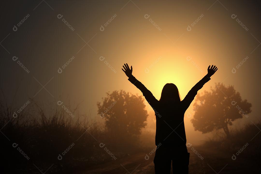 Silhouette of woman freedom travelers standing with arms raised and enjoying beautiful nature and cheering young people at sunset and fog