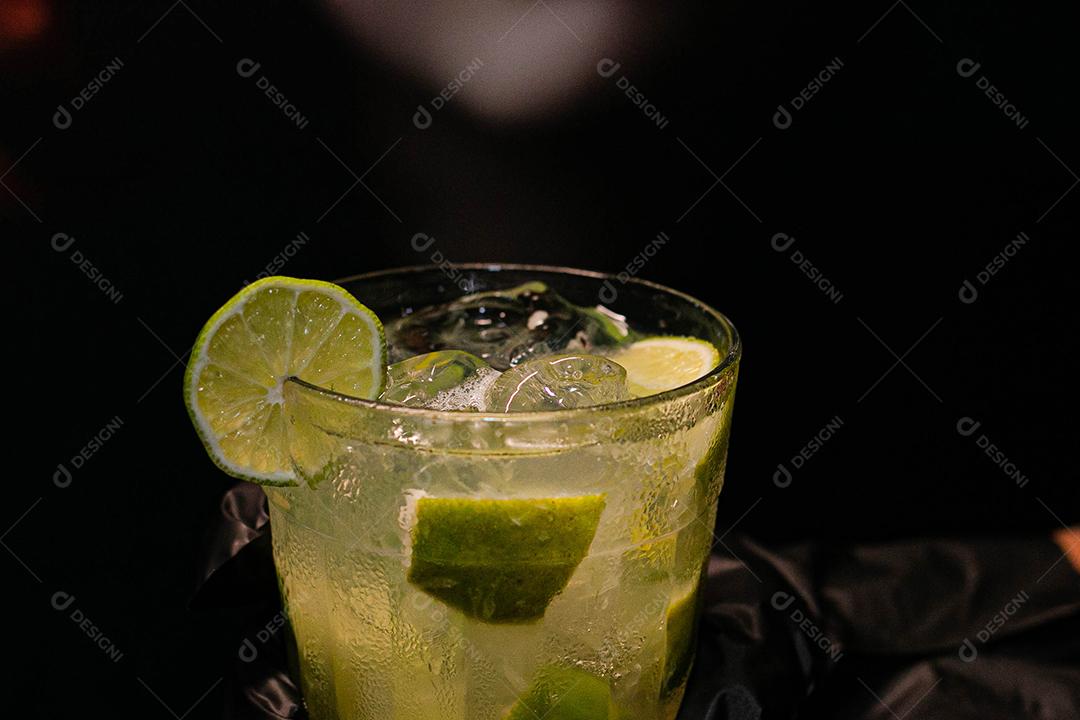 Caipirinha de limão com cubos de gelo em fundo preto