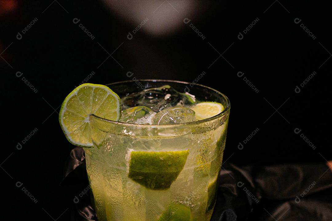Caipirinha de limão com cubos de gelo em fundo preto