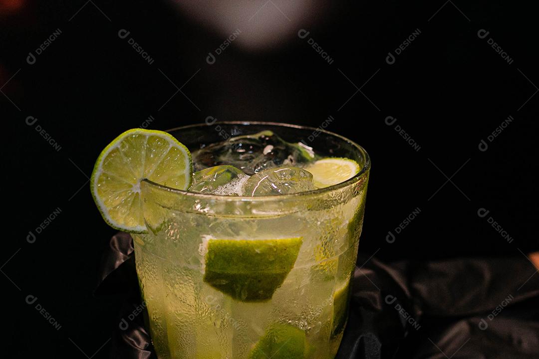 Caipirinha de limão com cubos de gelo em fundo preto