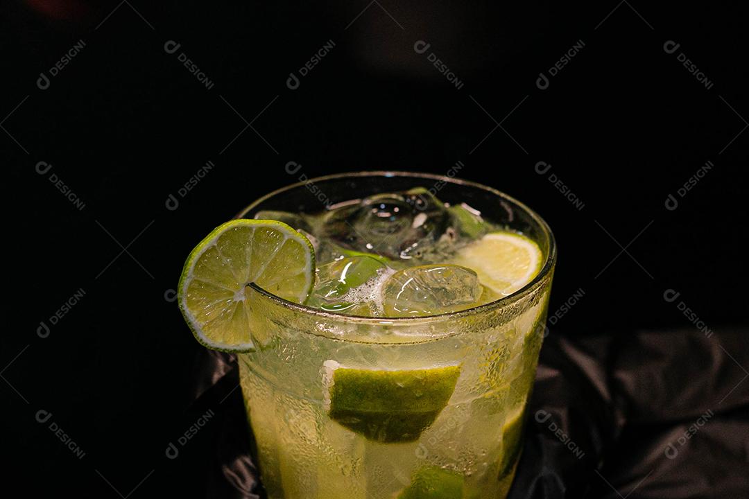 Caipirinha de limão com cubos de gelo em fundo preto