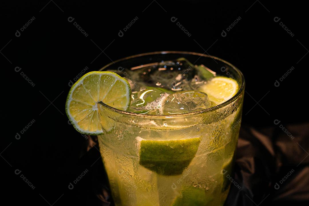 Caipirinha de limão com cubos de gelo em fundo preto