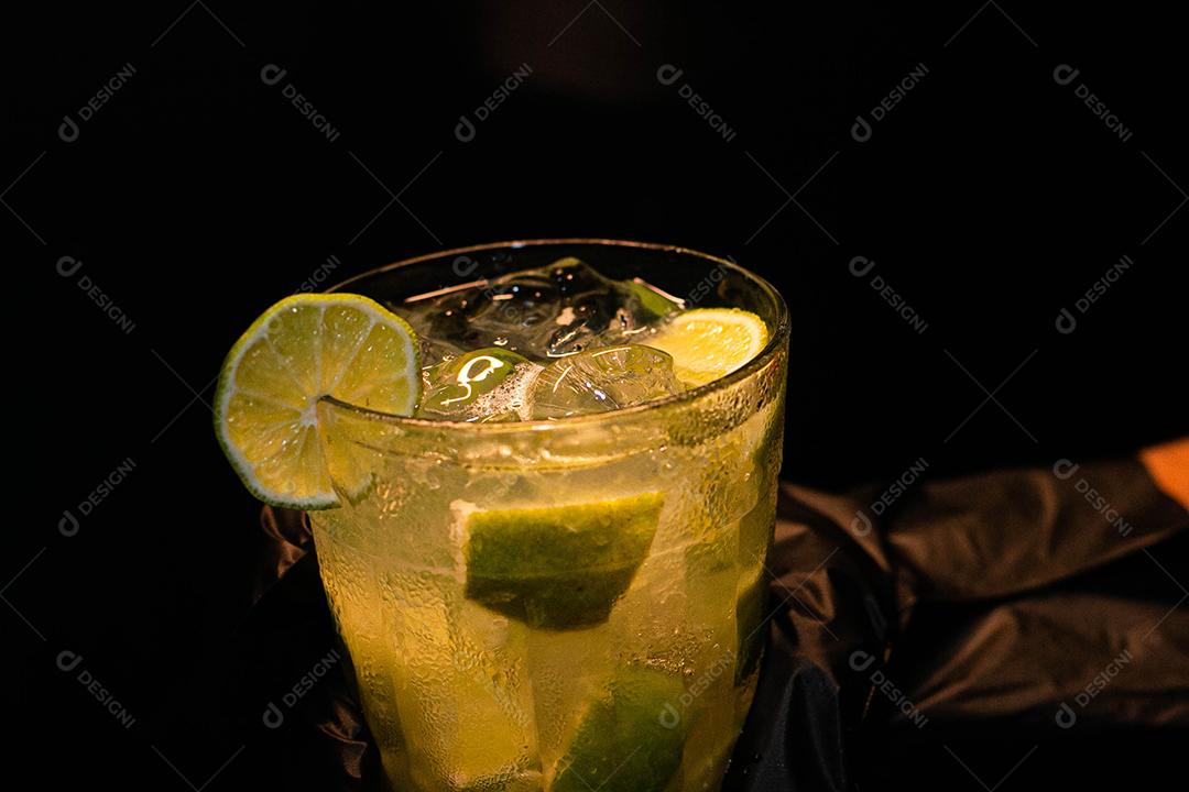 Caipirinha de limão com cubos de gelo em fundo preto
