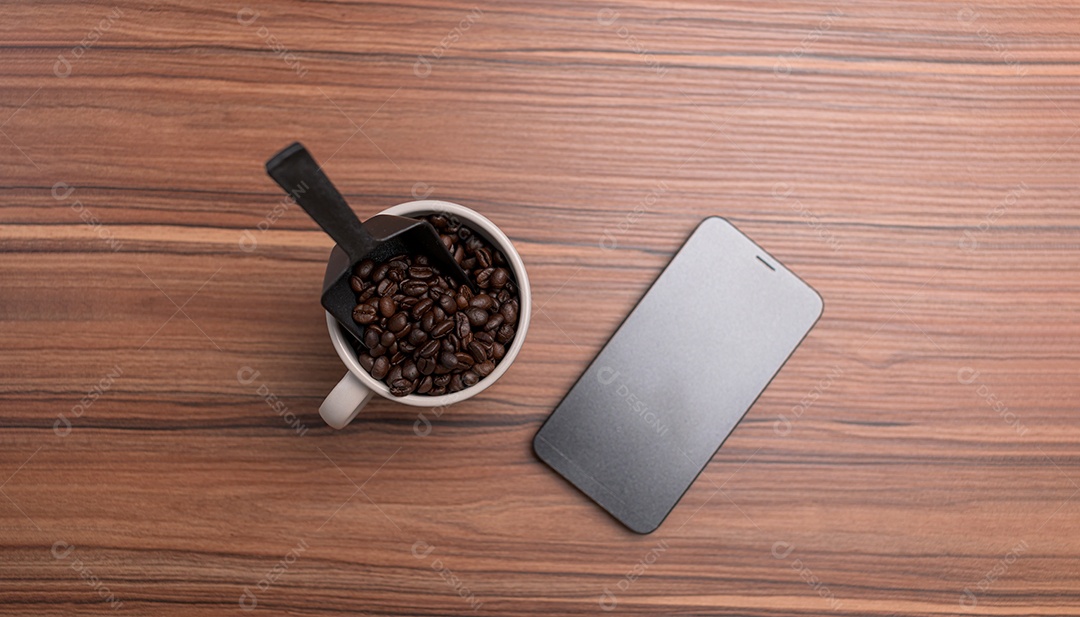 Xícara de grãos de café e um telefone estão na mesa.