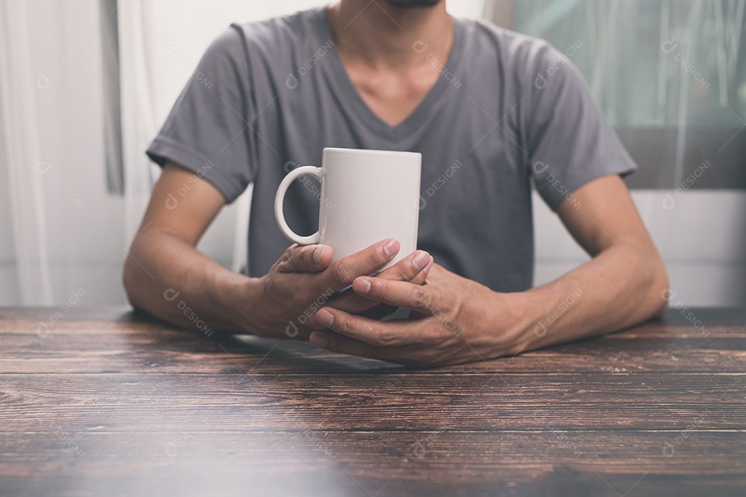Homem segurando um copo dágua, uma caneca de café, sobre uma mesa, em seu escritório.