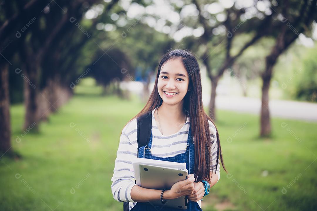 bela estudante asiática segurando livros e sorrindo para a câmera e conceito de aprendizagem e educação no parque