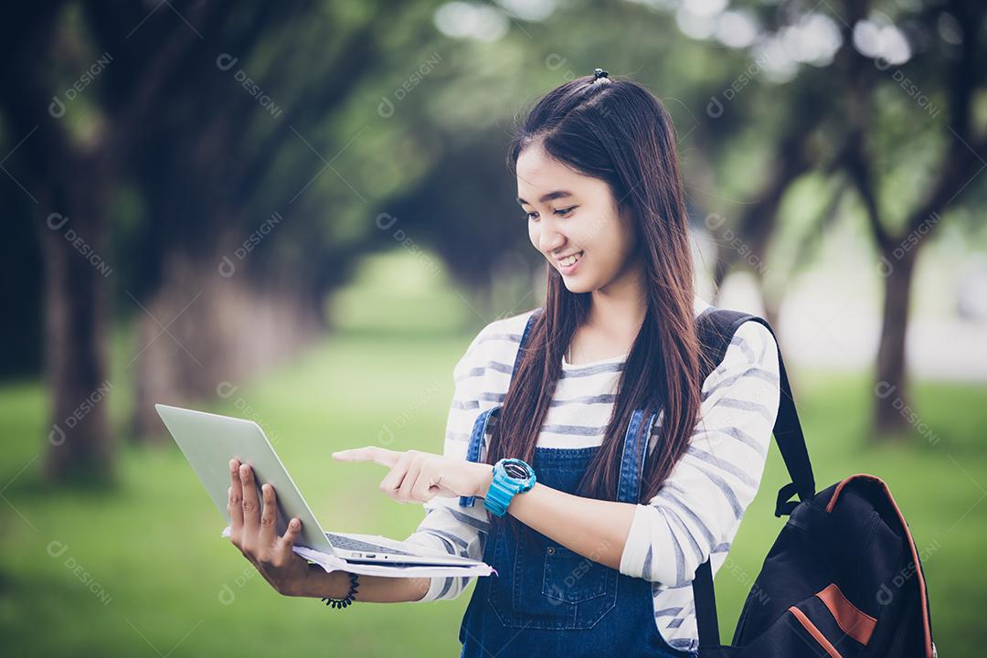 bela estudante asiática segurando livros e sorrindo para a câmera e conceito de aprendizagem e educação no parque