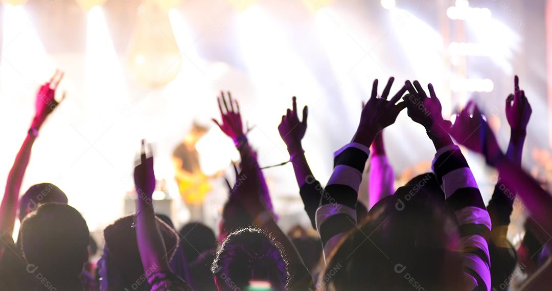 silhuetas da multidão do concerto na vista traseira da multidão do festival levantando as mãos nas luzes brilhantes do palco