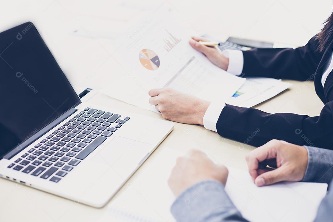 Empresária asiática segurando uma caneta e documentos de análise na mesa de escritório com computador