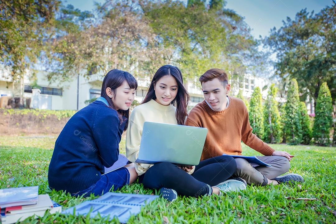Grupo de estudantes universitários asiáticos sentados na grama verde trabalhando e lendo fora juntos em um parque