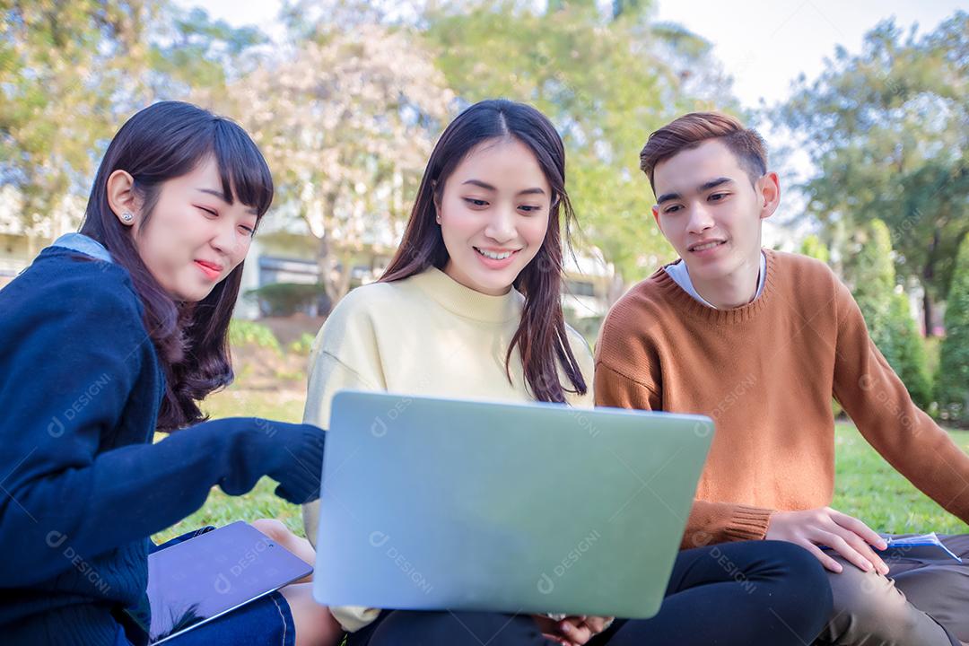 Grupo de estudantes universitários asiáticos sentados na grama verde trabalhando e lendo fora juntos em um parque