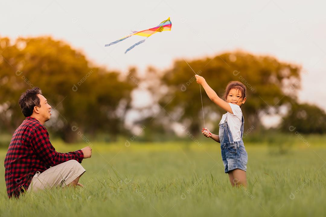 Asian girl and father with a kite running and happy in the meadow in summer in nature