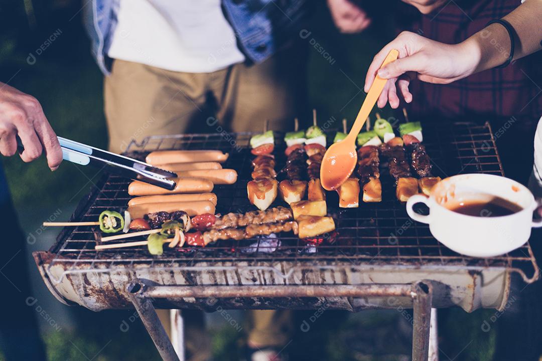Grupo asiático de amigos fazendo churrasco de jardim ao ar livre rindo com bebidas alcoólicas de cerveja à noite