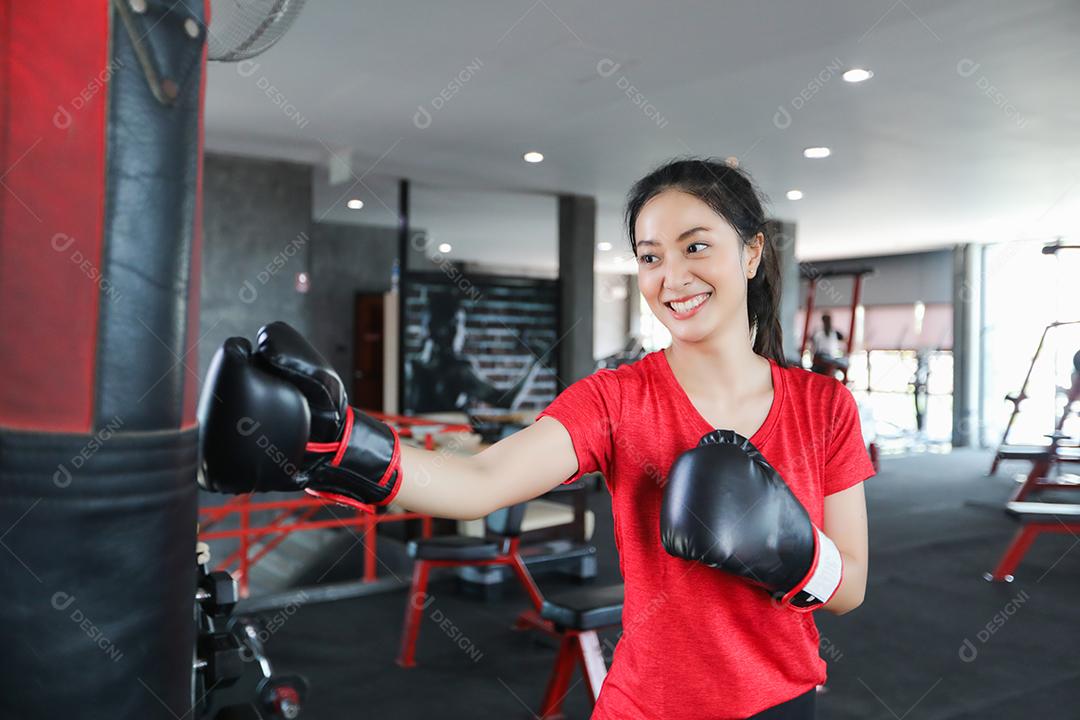 Mulher bonita boxer asiático feliz e divertido fitness boxe e socando um saco com luvas de boxe vestindo.