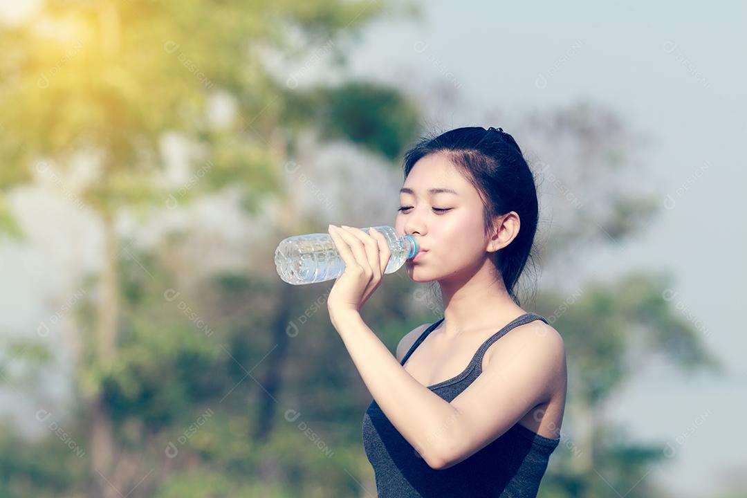 Mulher desportiva ásia segurando e bebendo água ao ar livre em dia ensolarado