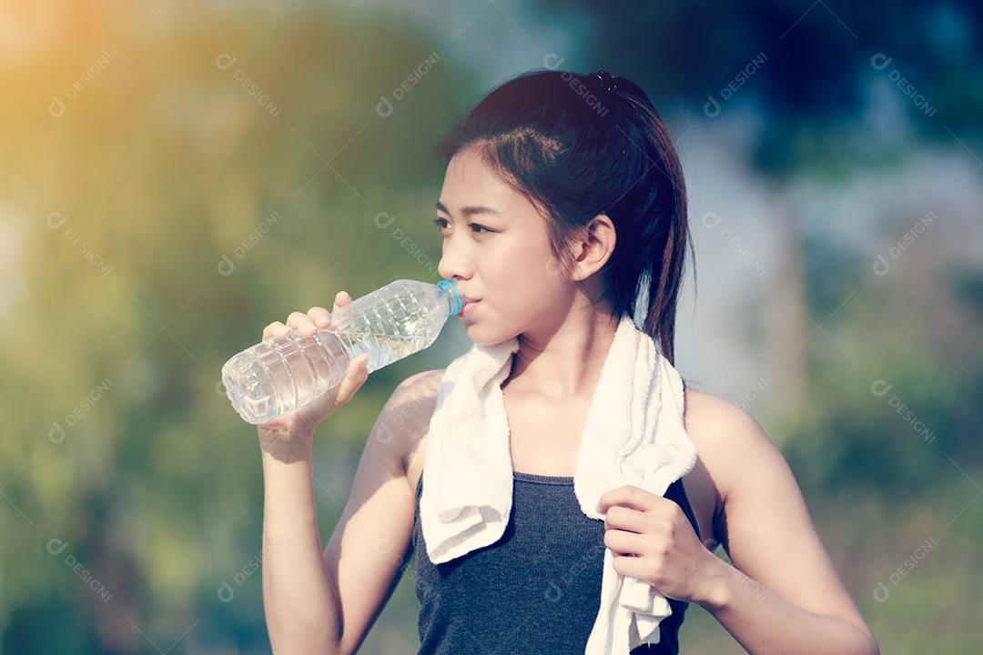 Mulher desportiva ásia segurando e bebendo água ao ar livre em dia ensolarado