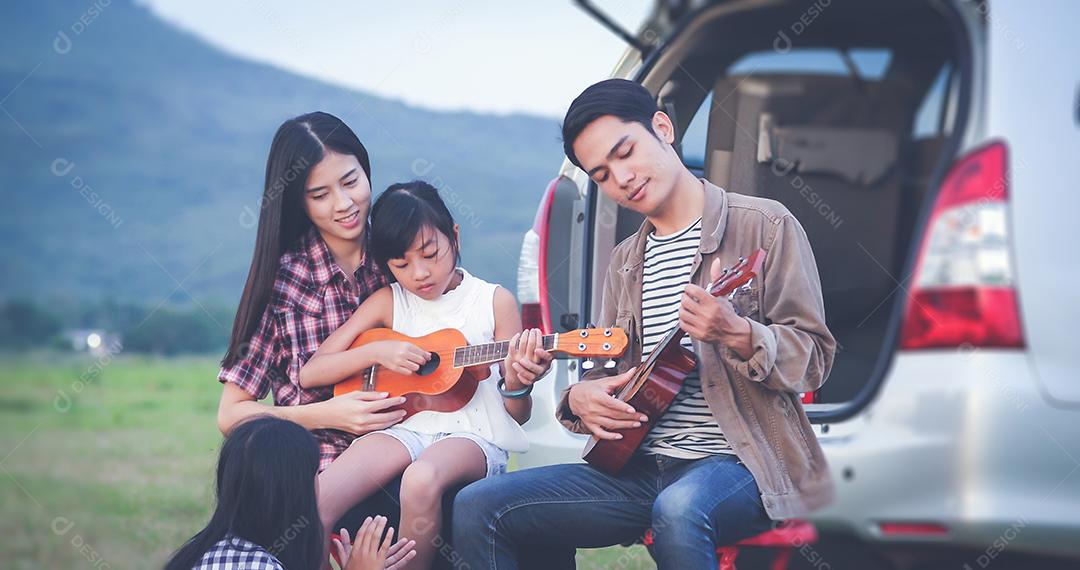 menina feliz tocando ukulele com família asiática sentado no carro para desfrutar de viagem e férias de verão