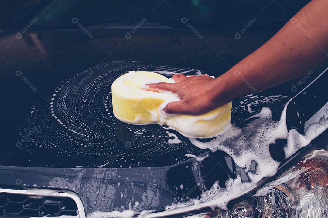 Homem usam uma esponja amarela para lavar o carro