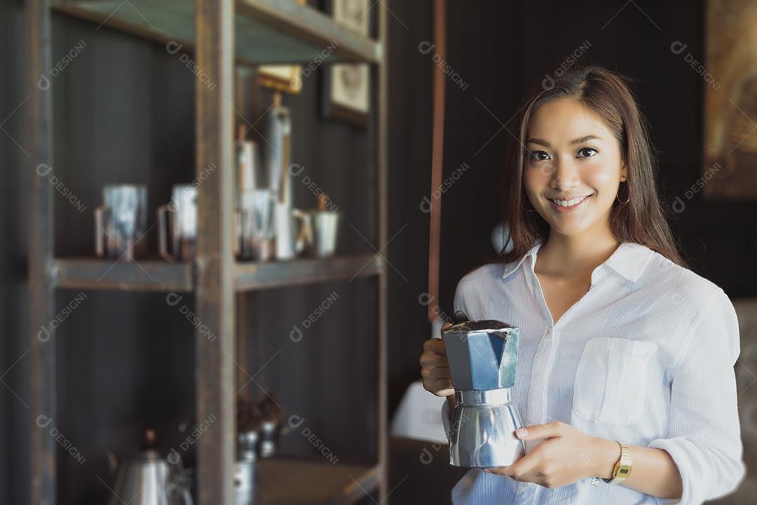Menina asiática em pé segurando uma cafeteira Sorria e divirta-se Relaxando em uma cafeteria