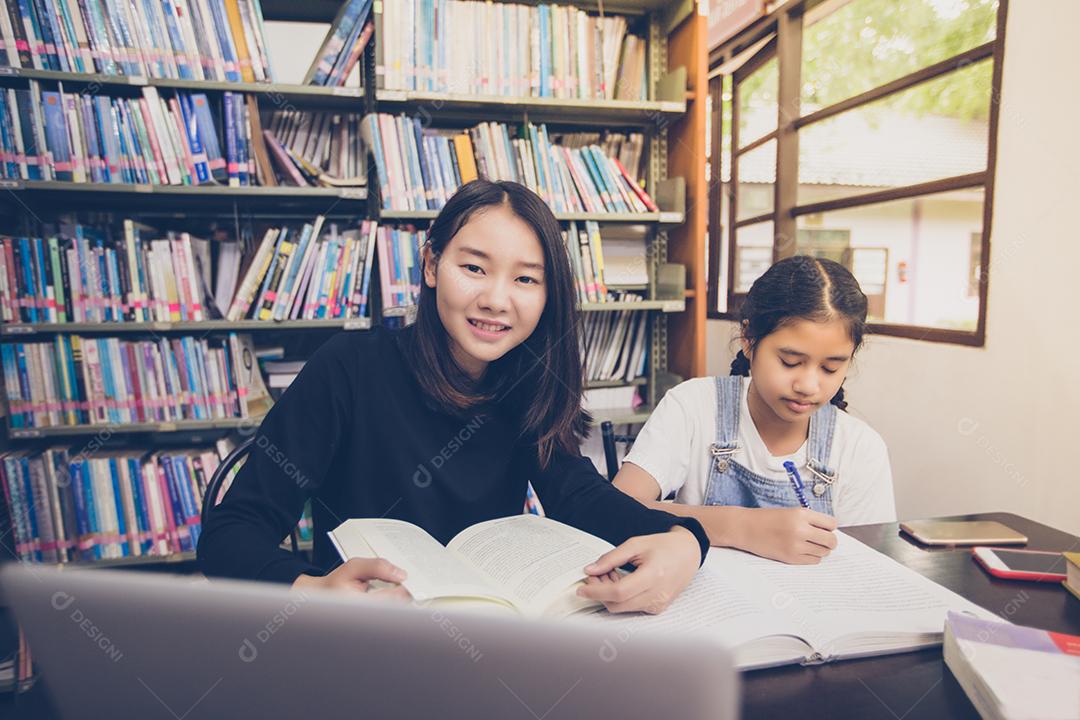 Estudantes asiáticos lendo livros na biblioteca.