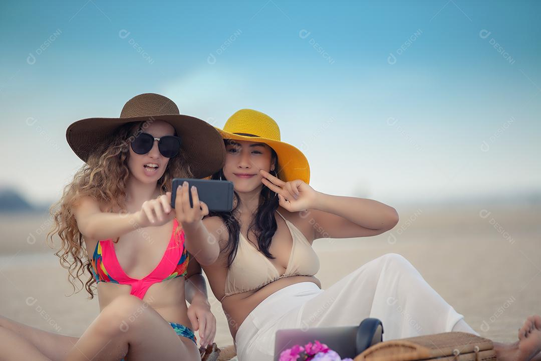 Mulheres estão tirando fotos e selfie com amigos na praia de areia no verão.