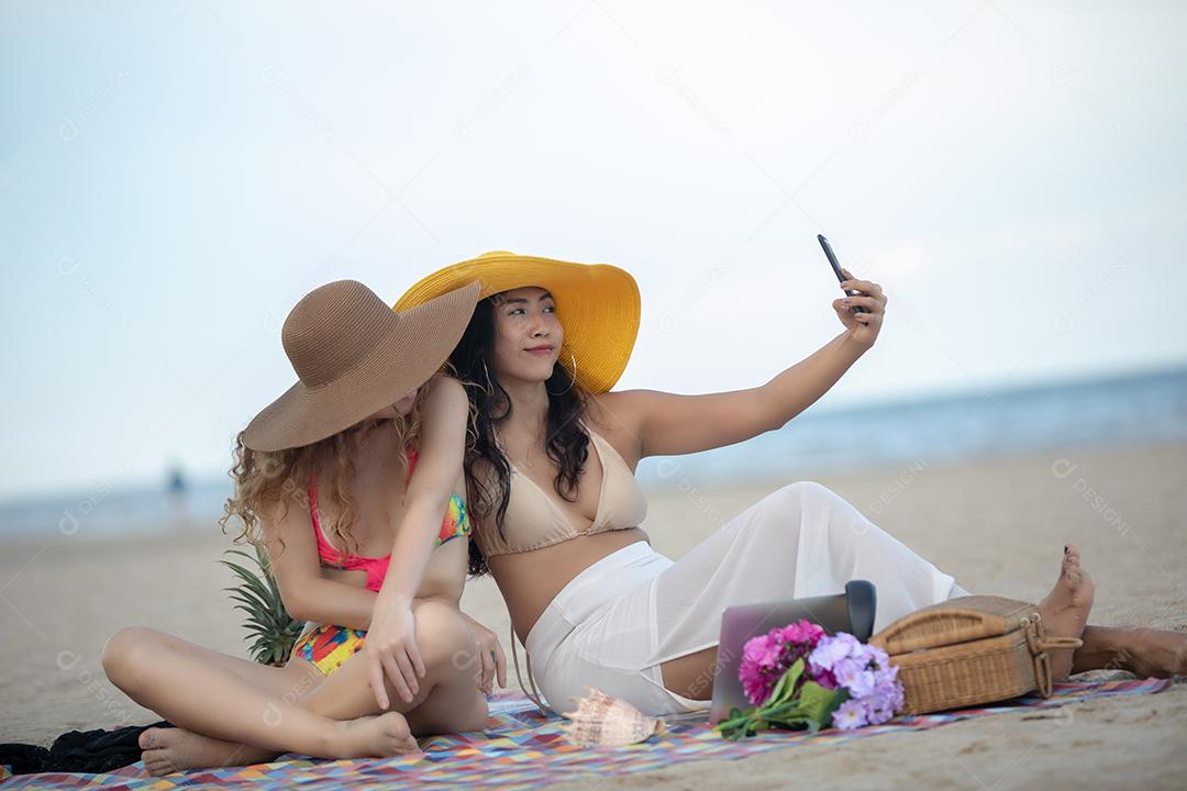 Mulheres estão tirando fotos e selfie com amigos na praia de areia no verão.