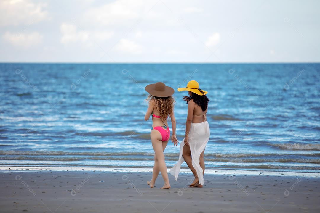 Mulheres vestindo biquínis estão andando com amigos na praia no verão.