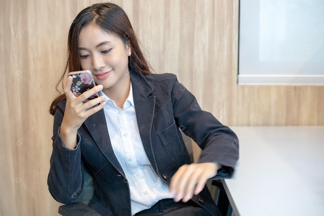 Mulher de negócios asiática usando telefone para celular e mensagens de texto em seu celular