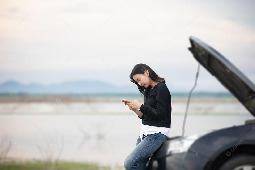 Mulher asiática usando telefone celular enquanto olha e homem estressado sentado após um colapso de carro na rua