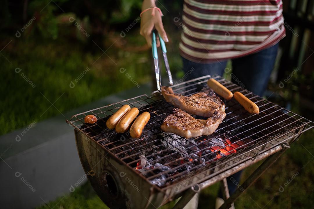 Grupo asiático de amigos fazendo churrasco de jardim ao ar livre rindo com bebidas alcoólicas de cerveja à noite