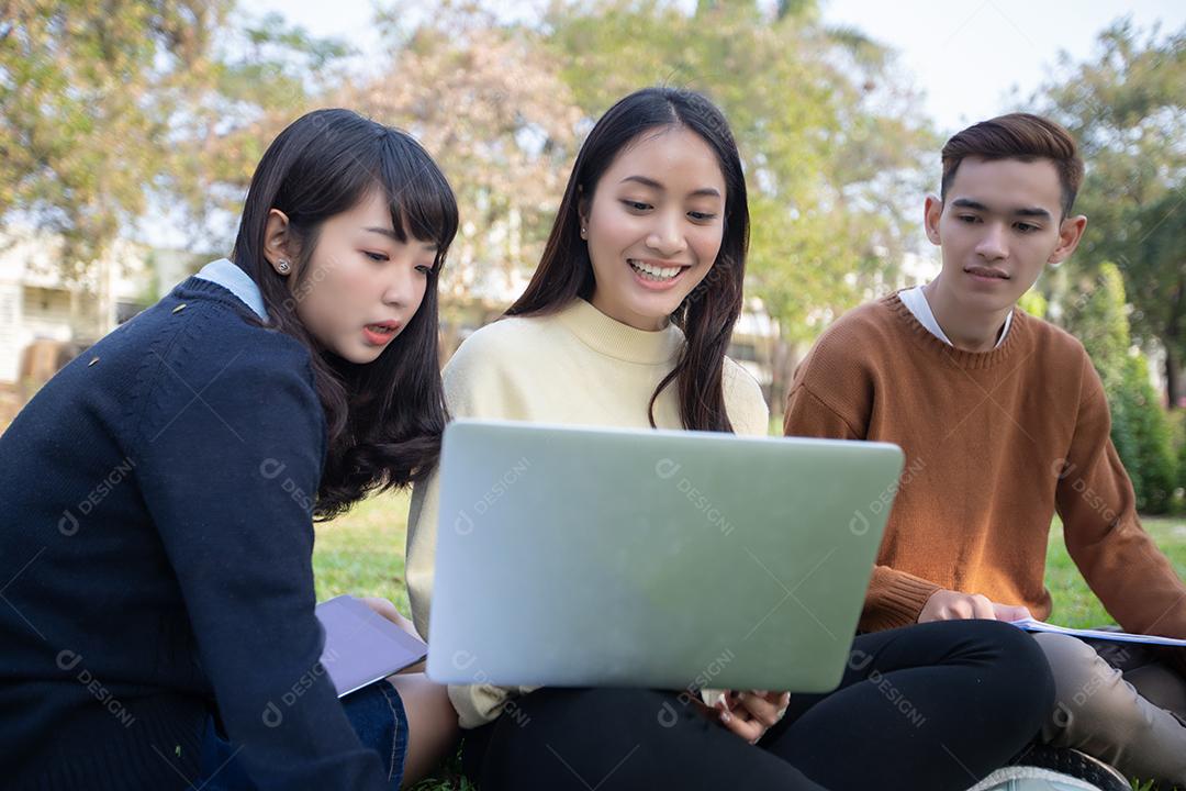 Grupo de estudantes universitários asiáticos sentados na grama verde trabalhando e lendo fora juntos em um parque