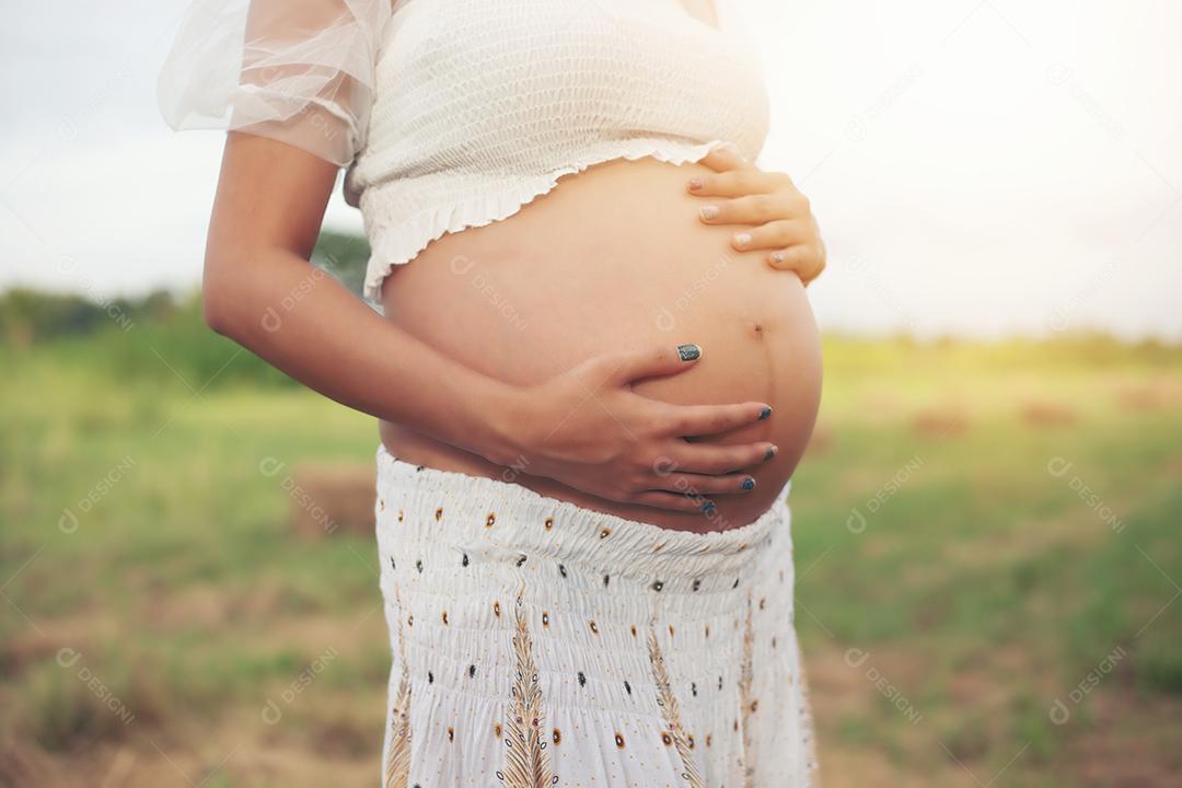 feliz e orgulhosa mulher asiática grávida olhando para sua barriga em um parque ao nascer do sol