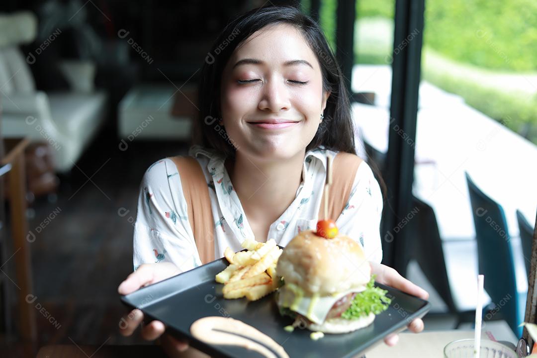 Mulheres asiáticas sorrindo e felizes e gostando de comer hambúrgueres no café e restaurante na hora do relaxamento