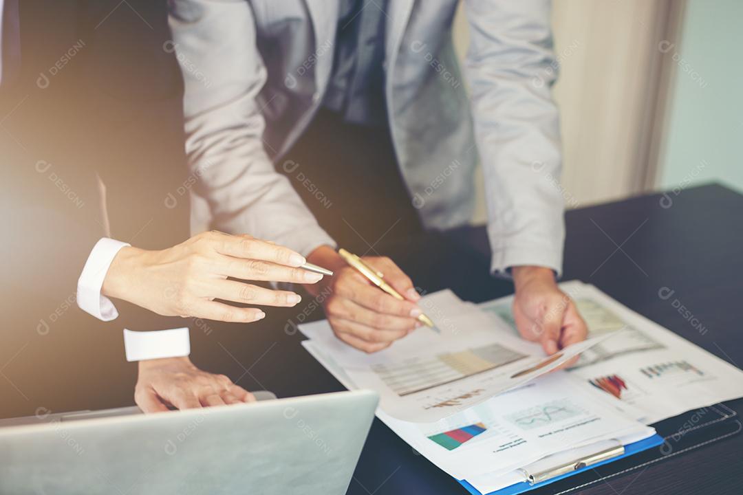 Empresárias asiáticas segurando uma caneta e documentos de análise na mesa de escritório com computador portátil e diagrama financeiro gráfico trabalhando em segundo plano