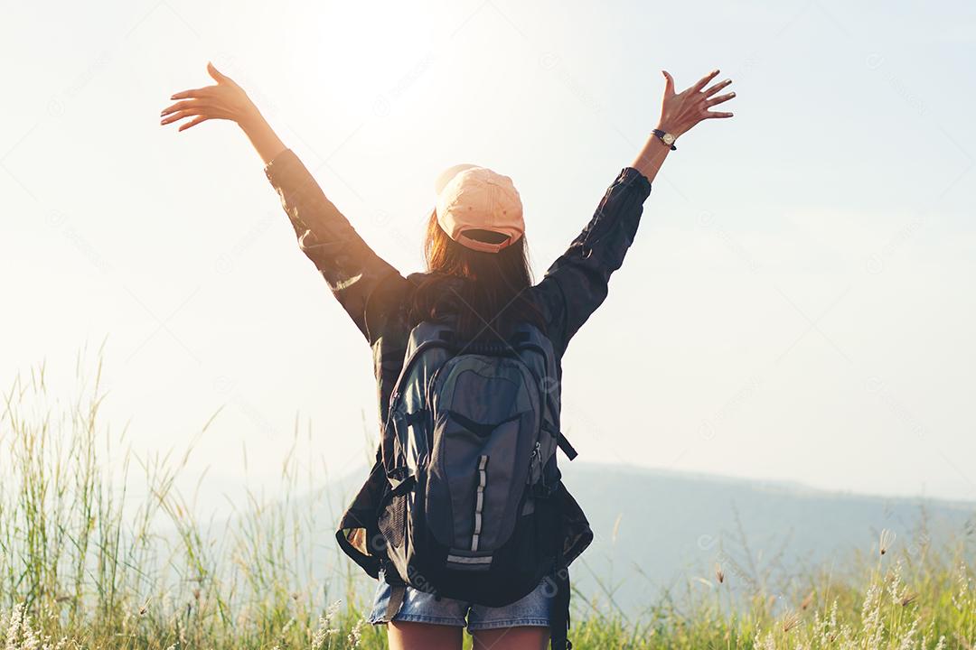 Mulher viajante da liberdade de pé com os braços levantados e desfrutando de uma bela natureza e torcendo o mochileiro jovem no pico da montanha à beira-mar do nascer do sol