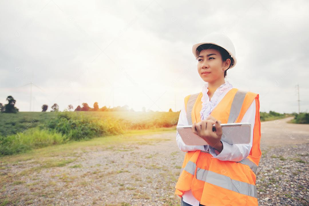 Engenheiro asiático com capacete usando computador tablet pc inspecionando e trabalhando na estação geradora de energia da fazenda de turbinas eólicas