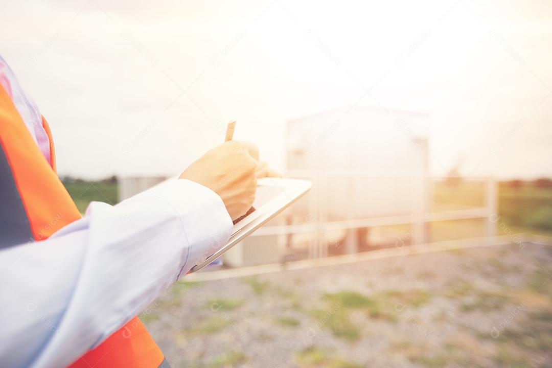 Engenheiro asiático com capacete usando computador tablet pc inspecionando e trabalhando na estação geradora de energia da fazenda de turbinas eólicas