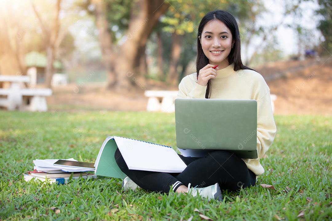 Mulher asiática Estudante universitário sorrindo e sentados na grama verde Trabalhando e lendo Fora Juntos em um parque