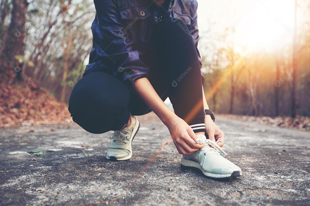 mulher amarrando cadarços para corredor de fitness esporte se preparando para correr ao ar livre no caminho da floresta no final do verão ou outono.