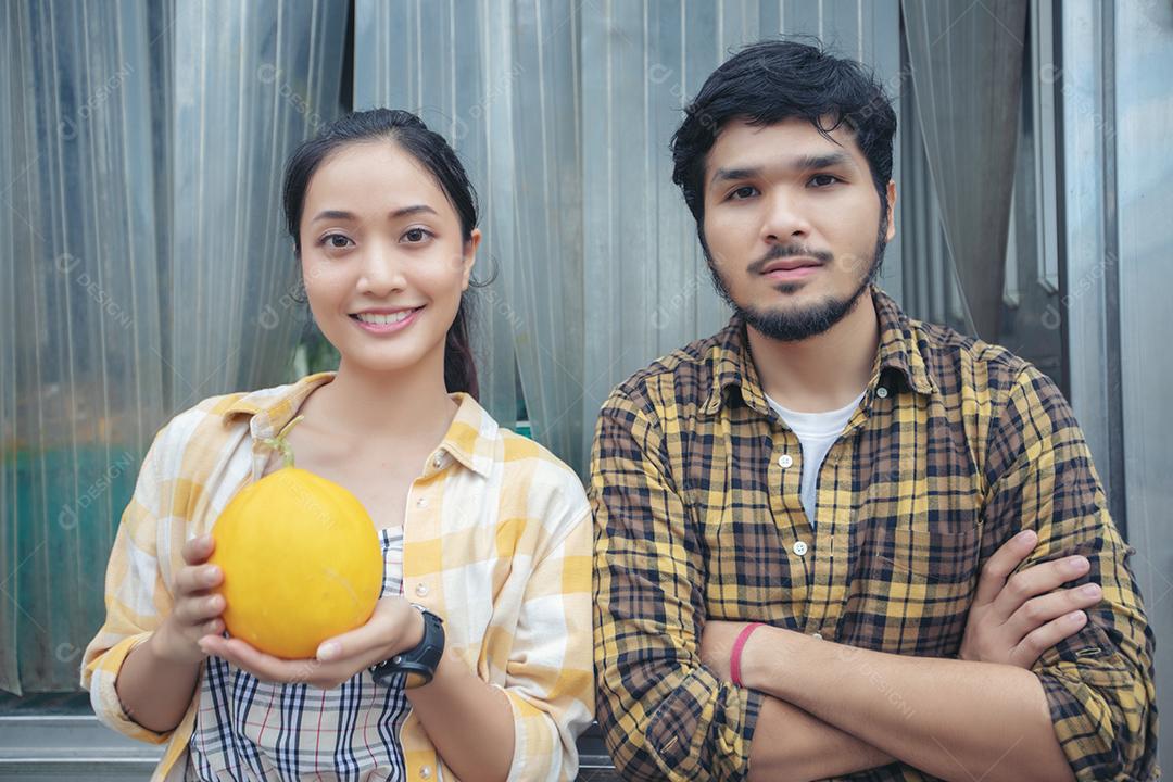 Dois fazendeiros estão segurando um melão e sorriem felizes na fazenda