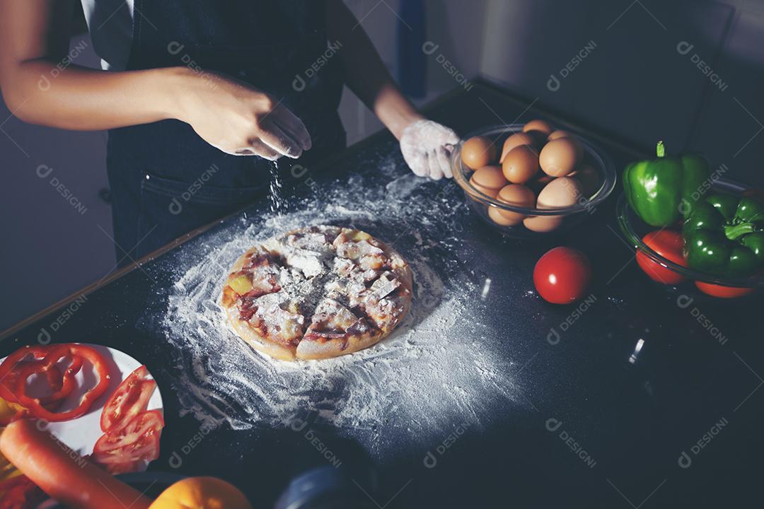 Mulheres asiáticas preparando uma pizza, amassando a massa e colocando ingredientes na mesa da cozinha