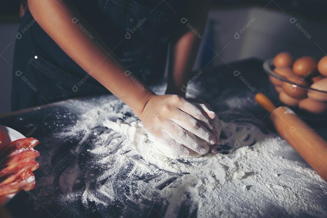 Mulheres asiáticas preparando uma pizza, amassando a massa e colocando ingredientes na mesa da cozinha